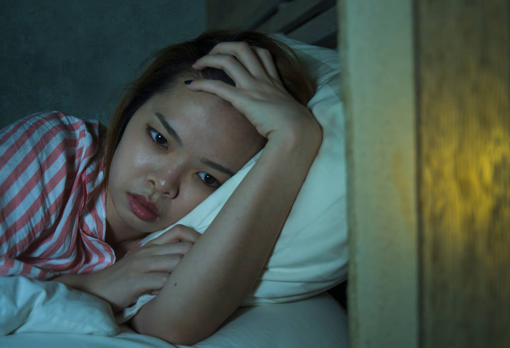 年轻美丽的悲伤和郁闷的亚洲中国女孩躺在床上深夜醒着看着想失眠睡眠
