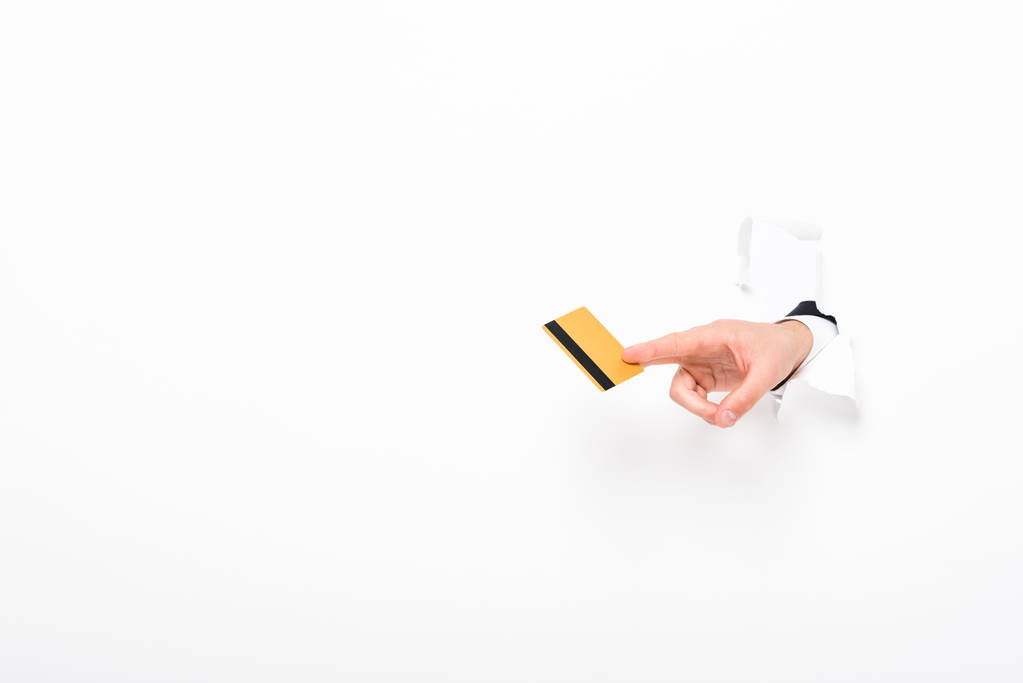 部分视图的人持有信用卡从墙上的洞在白色与复制空间