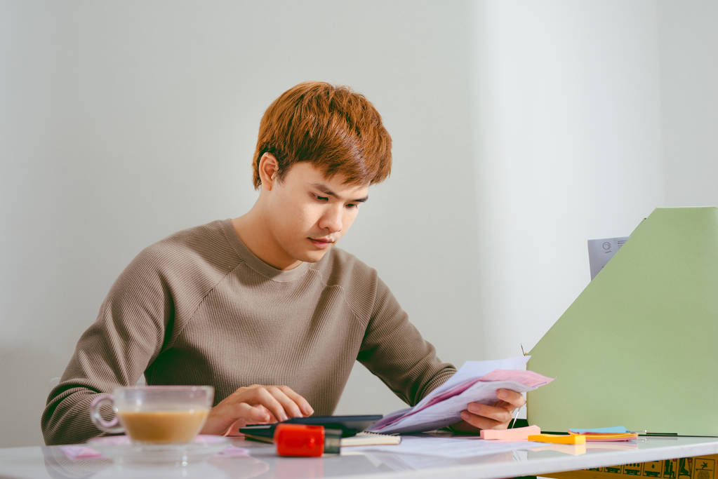 压力重重的亚洲人通过文书工作，计算开支，试图节省一些钱，管理财务，坐在桌子上与笔记本电脑，试图制定财务计划